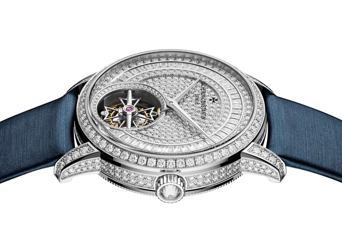 Điểm nhấn thiết kế là mặt số 39 mm chia tầng, đường viền thân vỏ khắc rãnh chìm, vành bezel mềm mại và khoá cài. Dây đeo xa-tanh màu xanh được lựa chọn tạo hiệu ứng tương phản, tôn vinh vẻ đẹp lộng lẫy.