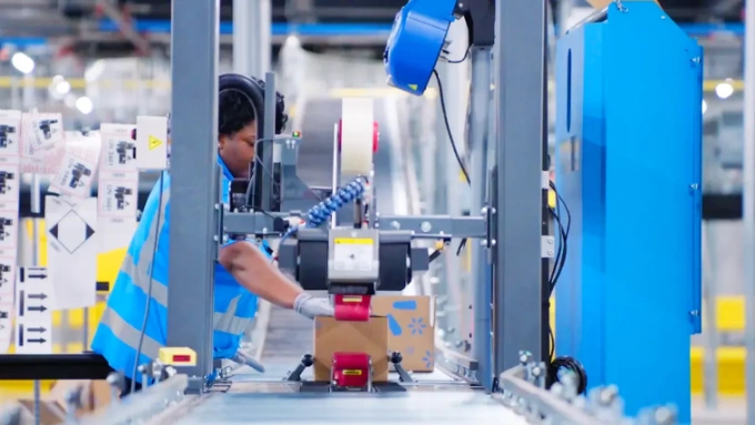 Một công nhân di chuyển một kiện hàng dọc theo băng chuyền đóng gói tại trung tâm phân phối Walmart ở Dallas-Fort Worth, Texas. Nhà bán lẻ này đang tận dụng công nghệ robot, thị giác máy tính và trí tuệ nhân tạo (AI) để tăng năng suất và an toàn kho bãi. Ảnh: Walmart